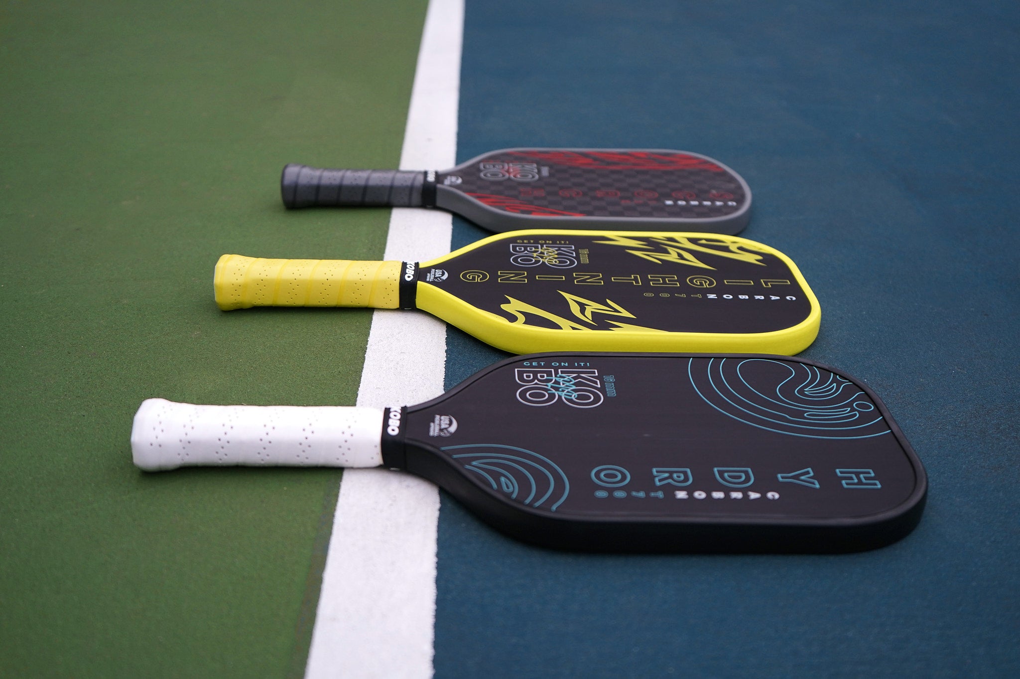 Three pickleball paddles on a court surface