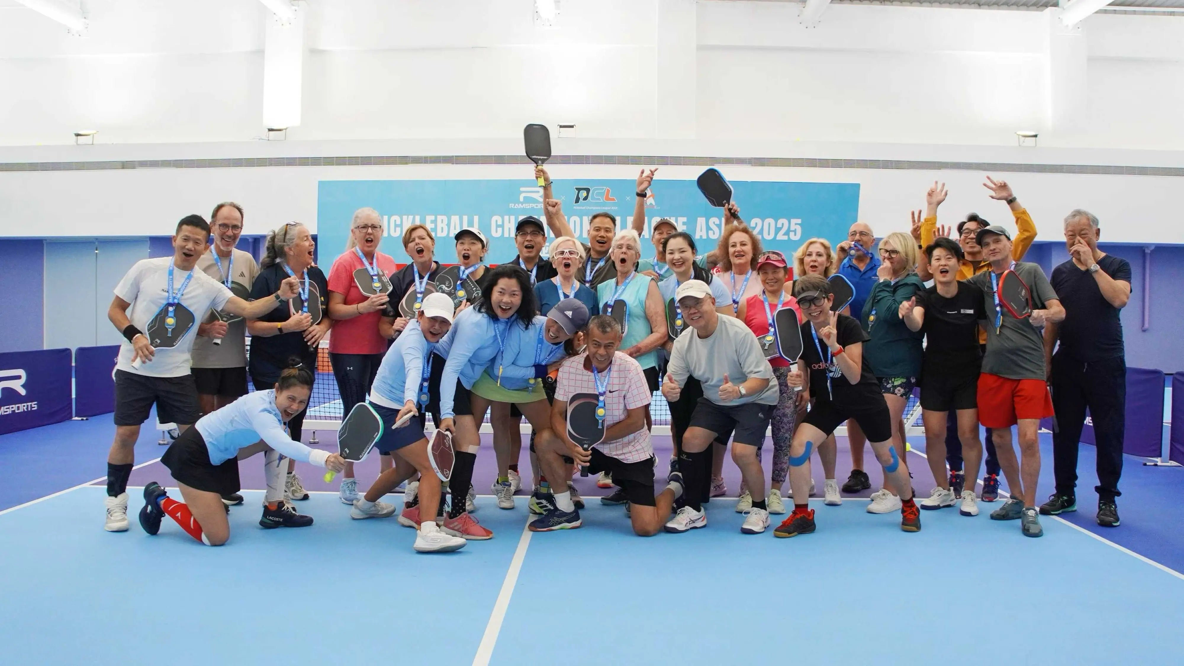 Indoor community pickleball tournament in Shenzhen, China, showing players of different ages celebrating with paddles and medals, highlighting inclusivity and global growth of the sport.