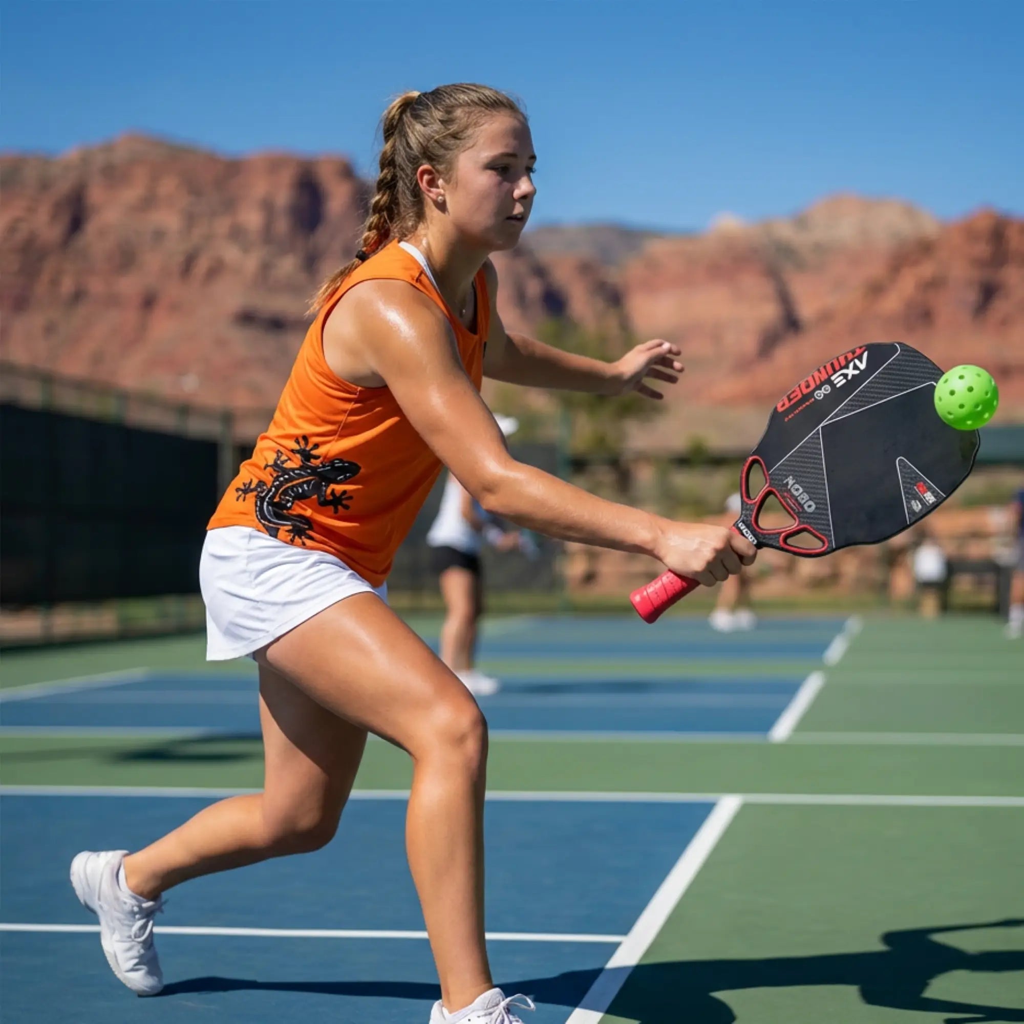 Woman playing pickleball on an outdoor court with mountains in the background with KOBO Thunder AXE Infinity pickleball paddle on her hand.